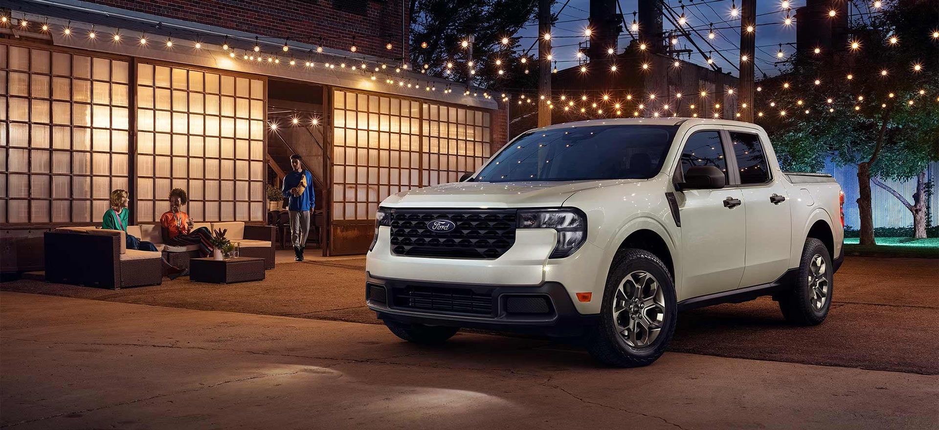 A white Ford Maverick® pickup parked in the forecourt of a restaurant at night.